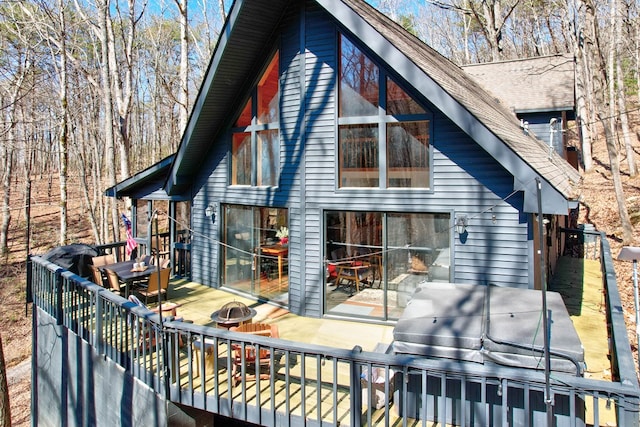 back of property with an outdoor fire pit, roof with shingles, and a deck