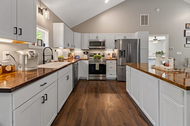 kitchen with appliances with stainless steel finishes, high vaulted ceiling, wood counters, white cabinetry, and sink