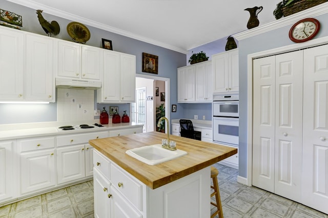 kitchen with white appliances, white cabinets, a center island, butcher block countertops, and sink