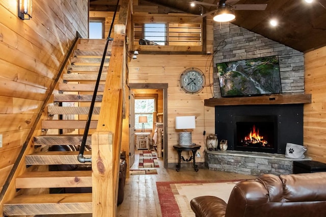 interior space with a stone fireplace, lofted ceiling, light wood-type flooring, and wooden walls