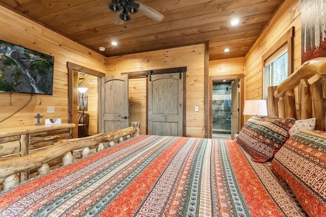 bedroom with wooden walls, ensuite bathroom, a barn door, wood ceiling, and ceiling fan