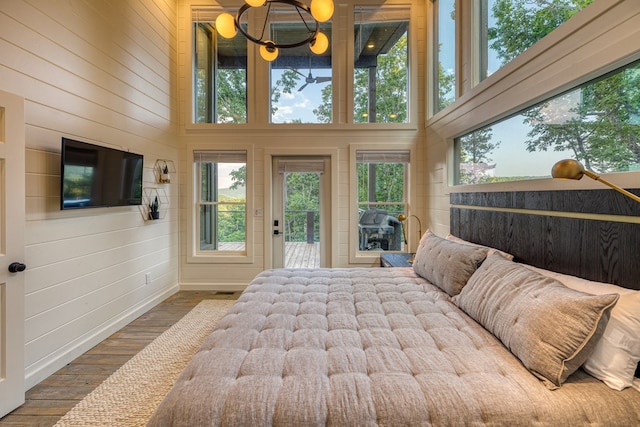 bedroom with wood walls, wood finished floors, a high ceiling, a notable chandelier, and access to outside