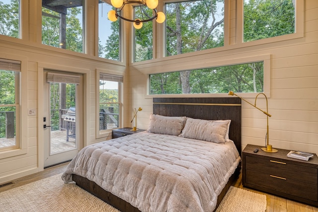 bedroom with access to outside, a chandelier, wood walls, and wood finished floors