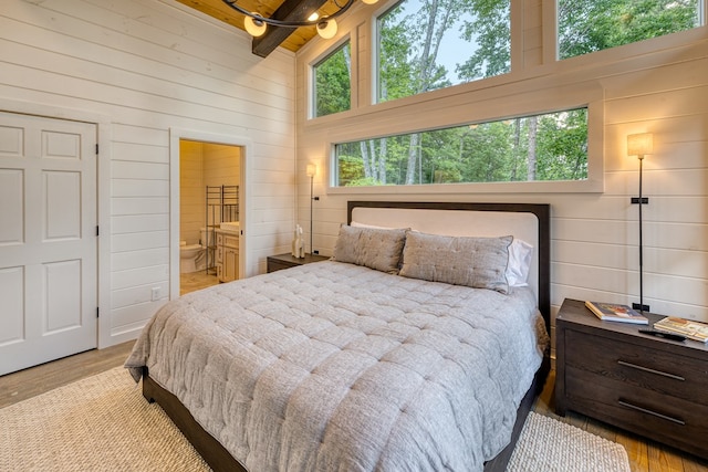 bedroom with ensuite bath, wood finished floors, wooden walls, and beamed ceiling