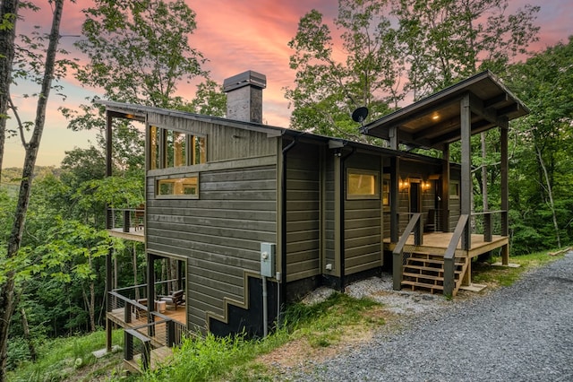 property exterior at dusk with a balcony, a chimney, and a deck