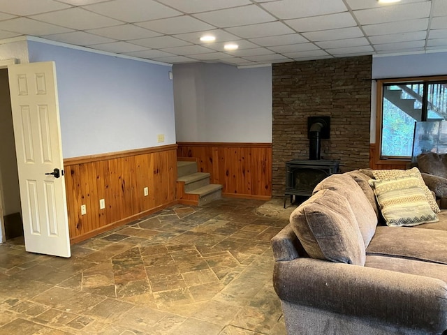 living room featuring a paneled ceiling, a wood stove, and wood walls