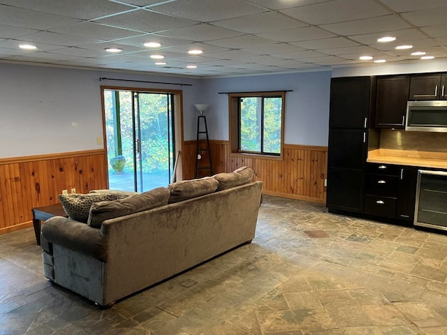 living room featuring wood walls, wine cooler, and a paneled ceiling