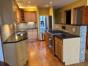 kitchen with sink, backsplash, appliances with stainless steel finishes, and light hardwood / wood-style flooring