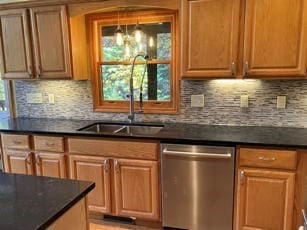 kitchen with stainless steel dishwasher, sink, dark stone counters, and backsplash