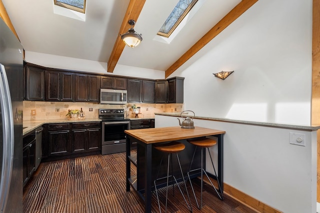 kitchen with decorative backsplash, lofted ceiling with skylight, dark brown cabinets, and appliances with stainless steel finishes