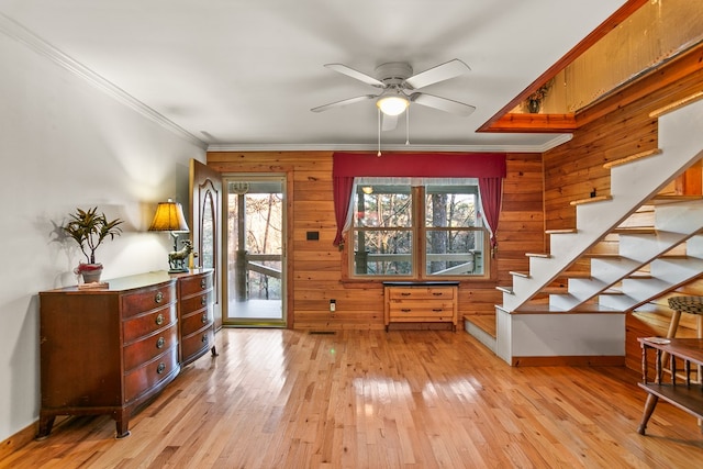 interior space featuring ceiling fan, light hardwood / wood-style floors, crown molding, and wooden walls