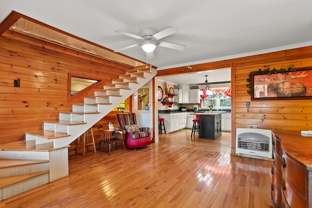 living room with light wood-type flooring, ornamental molding, heating unit, ceiling fan, and wooden walls