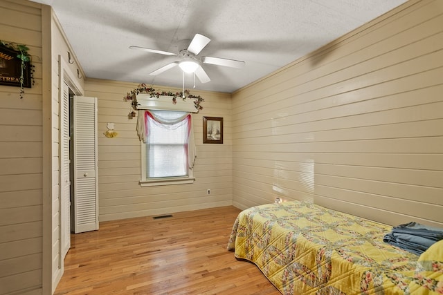 bedroom with a textured ceiling, light wood-type flooring, ceiling fan, and wood walls