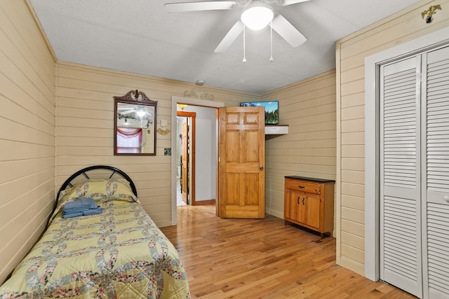 bedroom with a closet, ceiling fan, light hardwood / wood-style flooring, and wooden walls