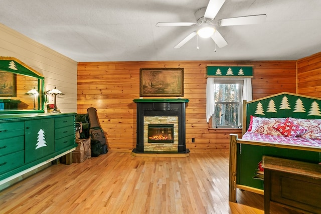 bedroom featuring light hardwood / wood-style floors, a stone fireplace, and wood walls