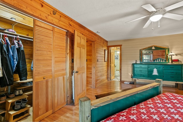 bedroom featuring a closet, ceiling fan, light hardwood / wood-style flooring, and wood walls