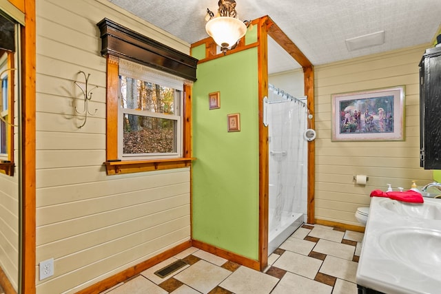 bathroom with vanity, a textured ceiling, toilet, curtained shower, and wood walls