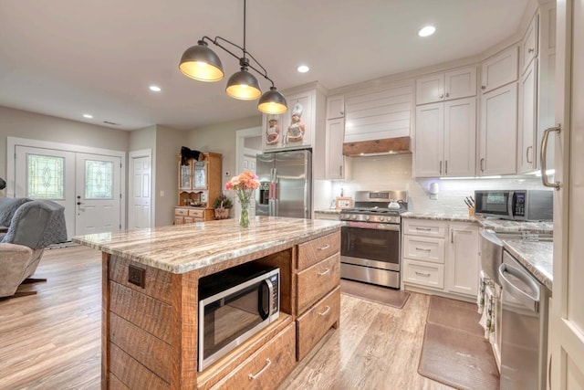 kitchen with hanging light fixtures, white cabinetry, a kitchen island, light stone countertops, and stainless steel appliances