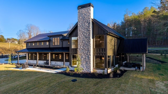 back of property featuring a chimney, stone siding, a lawn, board and batten siding, and metal roof