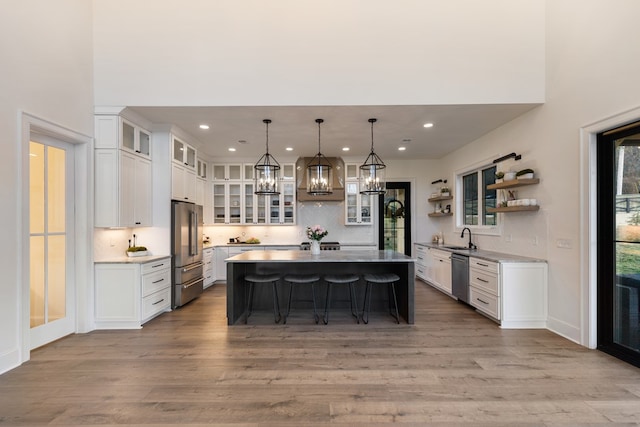 kitchen featuring a kitchen island, appliances with stainless steel finishes, wood finished floors, white cabinetry, and a sink