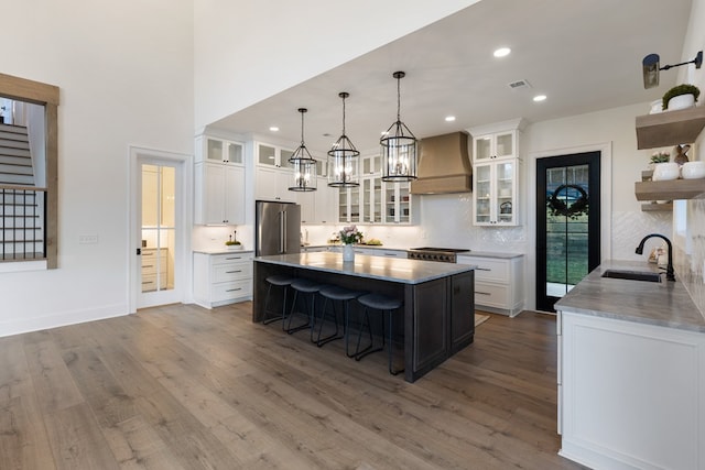 kitchen with high end fridge, a sink, open shelves, a kitchen breakfast bar, and custom exhaust hood
