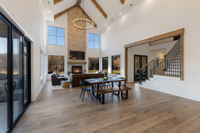 dining room with stairway, wood finished floors, an inviting chandelier, beam ceiling, and a fireplace