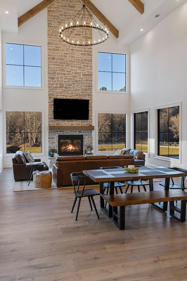 dining room with beamed ceiling, high vaulted ceiling, wood finished floors, an inviting chandelier, and a fireplace