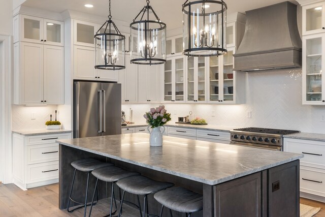 kitchen featuring high quality appliances, custom range hood, a kitchen island, white cabinetry, and a chandelier