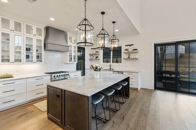 kitchen with a kitchen island, custom exhaust hood, open shelves, stainless steel stove, and a kitchen breakfast bar