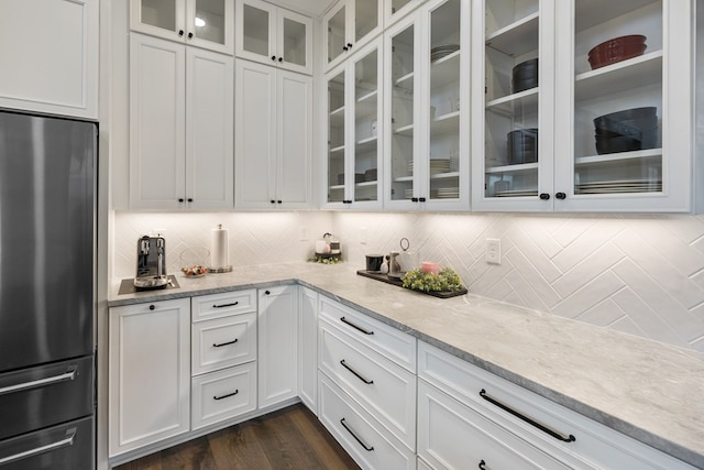 kitchen featuring white cabinets, light stone counters, glass insert cabinets, and freestanding refrigerator