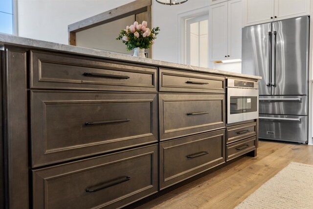 interior space featuring white cabinetry, freestanding refrigerator, light wood finished floors, light stone countertops, and dark brown cabinets
