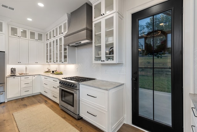 kitchen featuring wood finished floors, visible vents, premium range hood, white cabinets, and appliances with stainless steel finishes