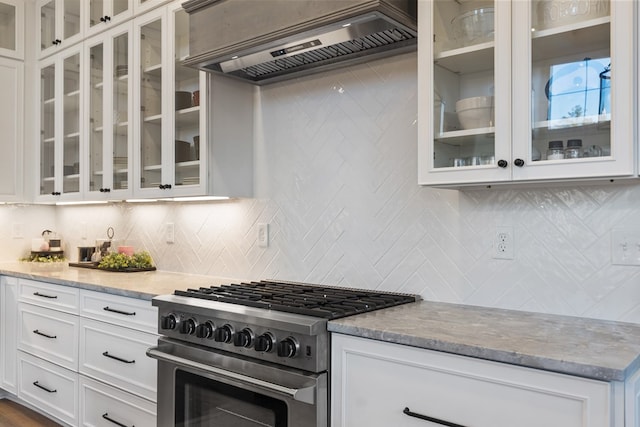 kitchen with custom exhaust hood, stainless steel range, white cabinetry, and light stone counters