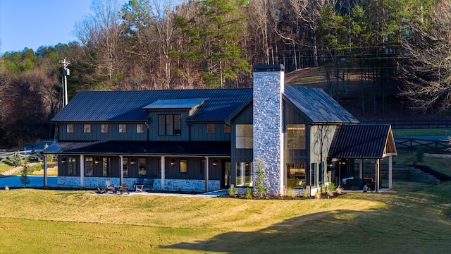 back of house with a yard, board and batten siding, metal roof, and a chimney