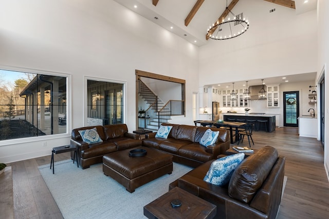 living room with beam ceiling, plenty of natural light, dark wood-style flooring, stairs, and a chandelier