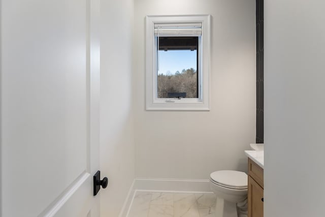 half bath with vanity, toilet, baseboards, and marble finish floor