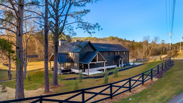 exterior space with board and batten siding, fence, a front yard, a chimney, and metal roof