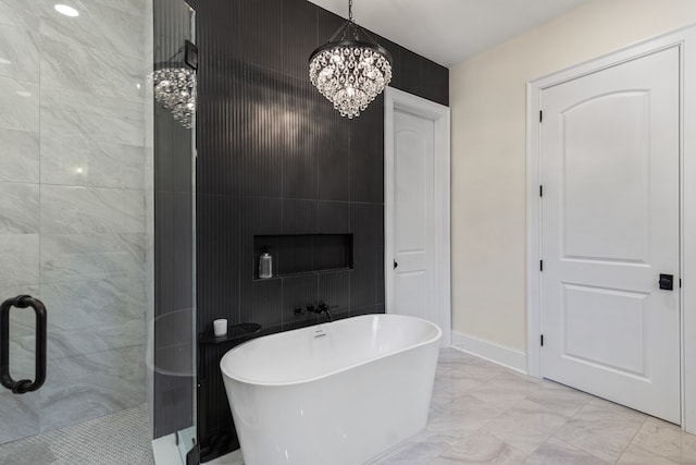 full bath featuring a notable chandelier, marble finish floor, a shower stall, baseboards, and a freestanding bath
