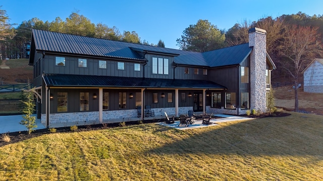 rear view of property with board and batten siding, a fire pit, a lawn, a chimney, and stone siding
