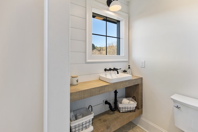 half bath featuring toilet, baseboards, and a sink