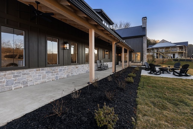 view of side of property with a patio, an outdoor fire pit, ceiling fan, a chimney, and a lawn