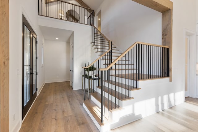 foyer entrance with hardwood / wood-style floors, stairs, baseboards, and a towering ceiling