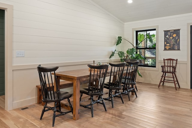 dining area with wooden walls, vaulted ceiling, and light hardwood / wood-style flooring