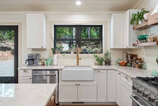 kitchen featuring appliances with stainless steel finishes, white cabinets, light stone countertops, and sink