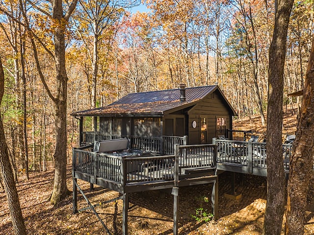 back of property featuring a wooden deck, a forest view, and metal roof