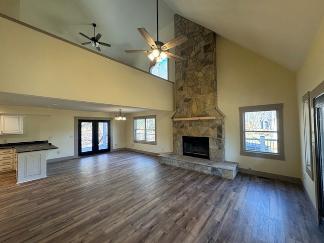 unfurnished living room with french doors, dark hardwood / wood-style flooring, ceiling fan with notable chandelier, high vaulted ceiling, and a fireplace