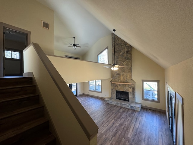 staircase featuring a textured ceiling, ceiling fan, wood-type flooring, high vaulted ceiling, and a stone fireplace