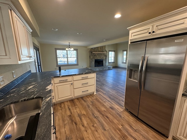 kitchen with a stone fireplace, dark hardwood / wood-style floors, stainless steel fridge, a wealth of natural light, and a notable chandelier