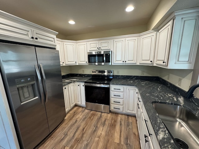 kitchen featuring sink, dark wood-type flooring, dark stone counters, white cabinets, and appliances with stainless steel finishes