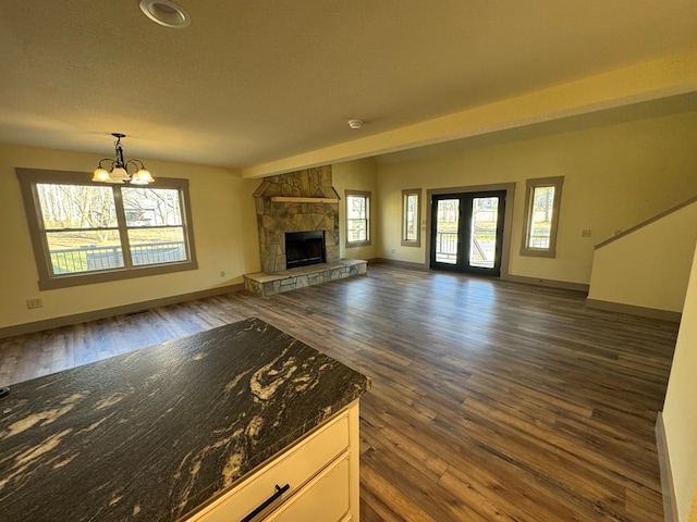 unfurnished living room featuring a notable chandelier, dark hardwood / wood-style floors, a fireplace, and french doors